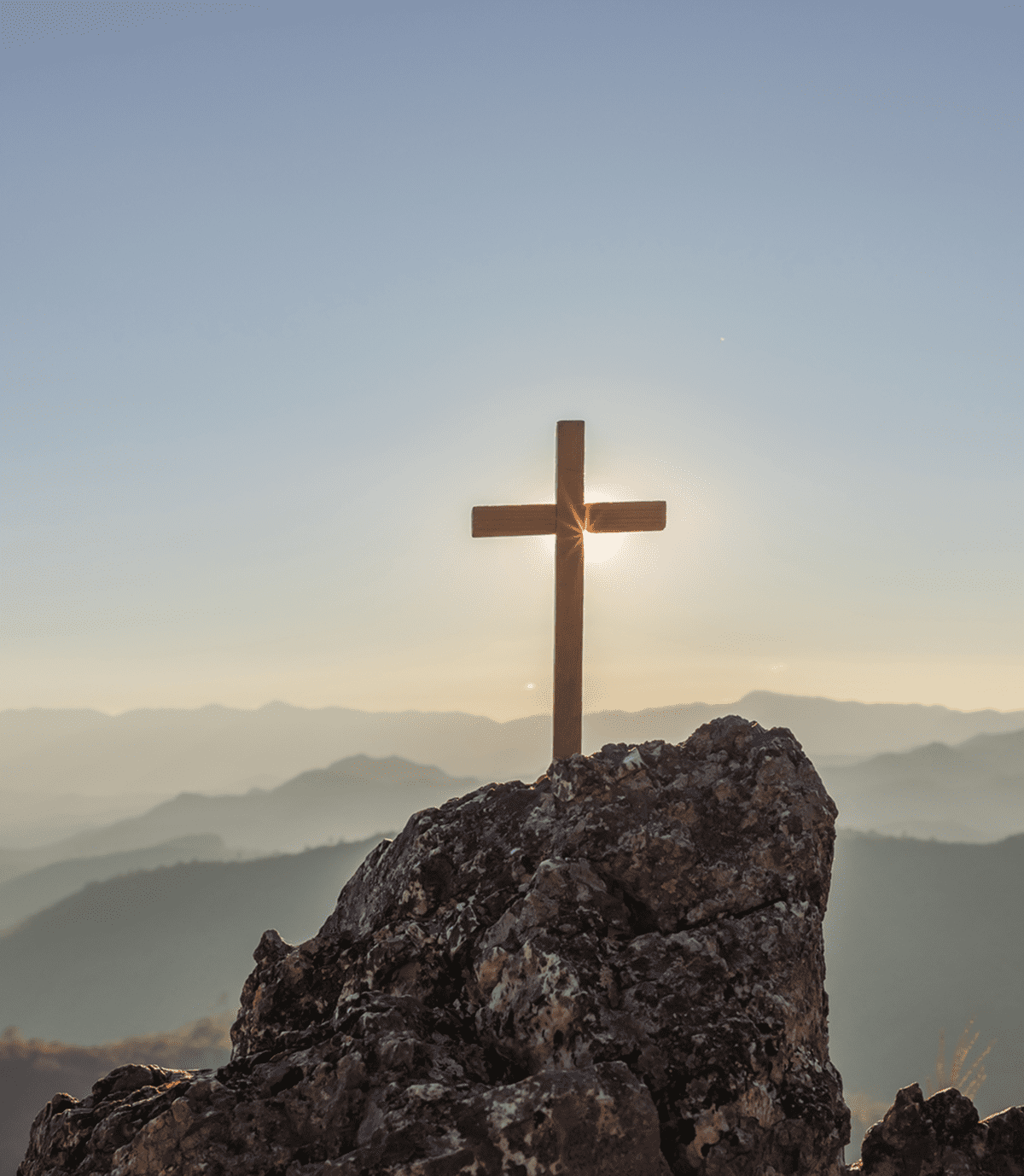 Sunlight through cross on rocky mountain